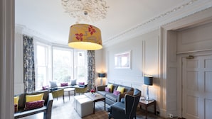 Un salon bien éclairé, avec un canapé, des fauteuils, une table basse et une lampe.