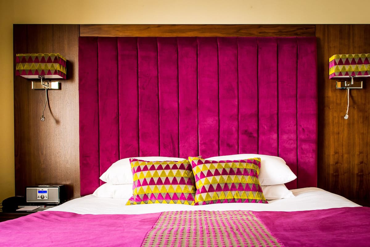 A hotel room with a large bed, a wooden headboard, and two wall-mounted lamps.