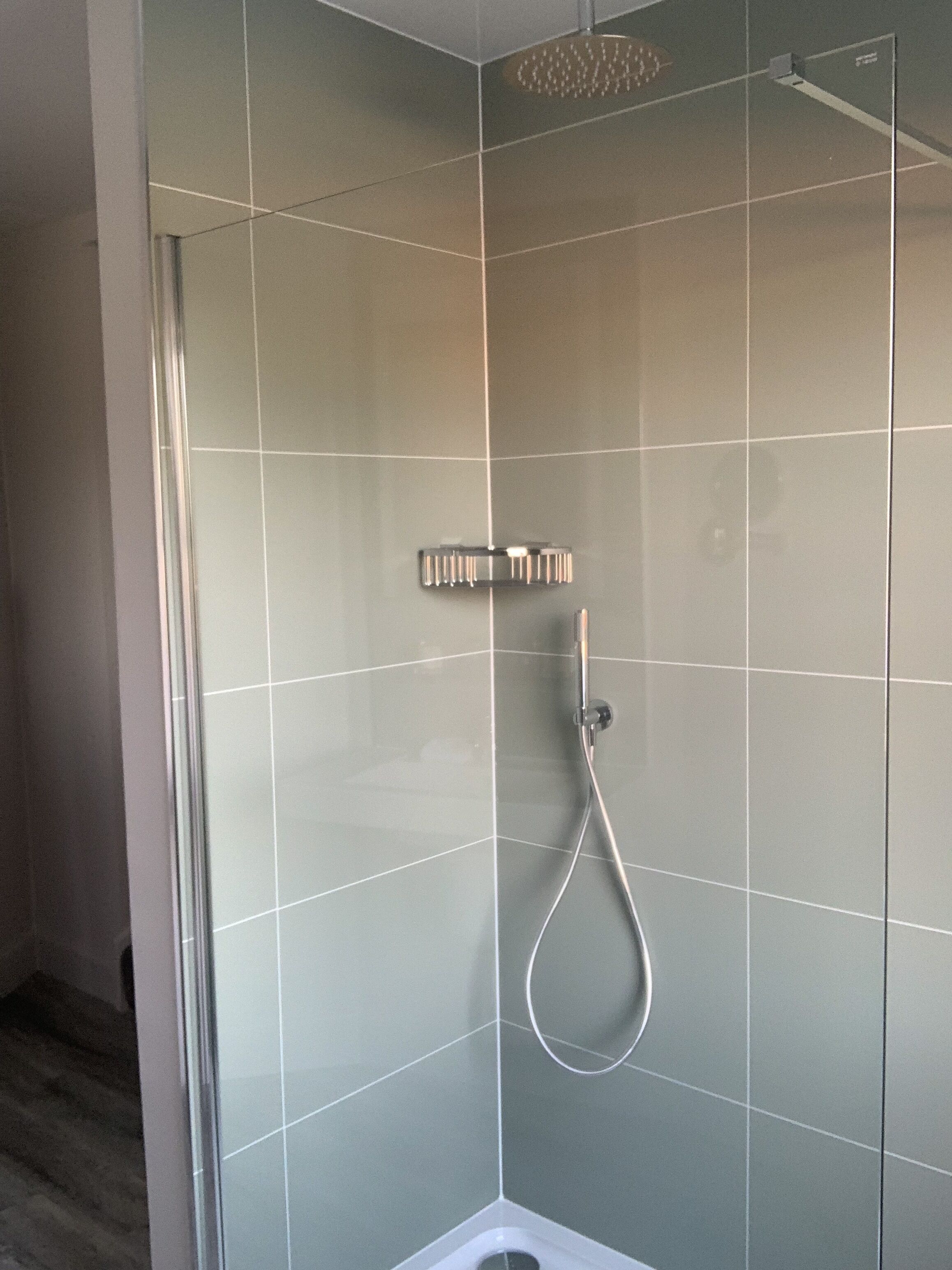 Un box de ducha moderno con puerta de cristal, cabezal de ducha manual y panel de control en la pared.