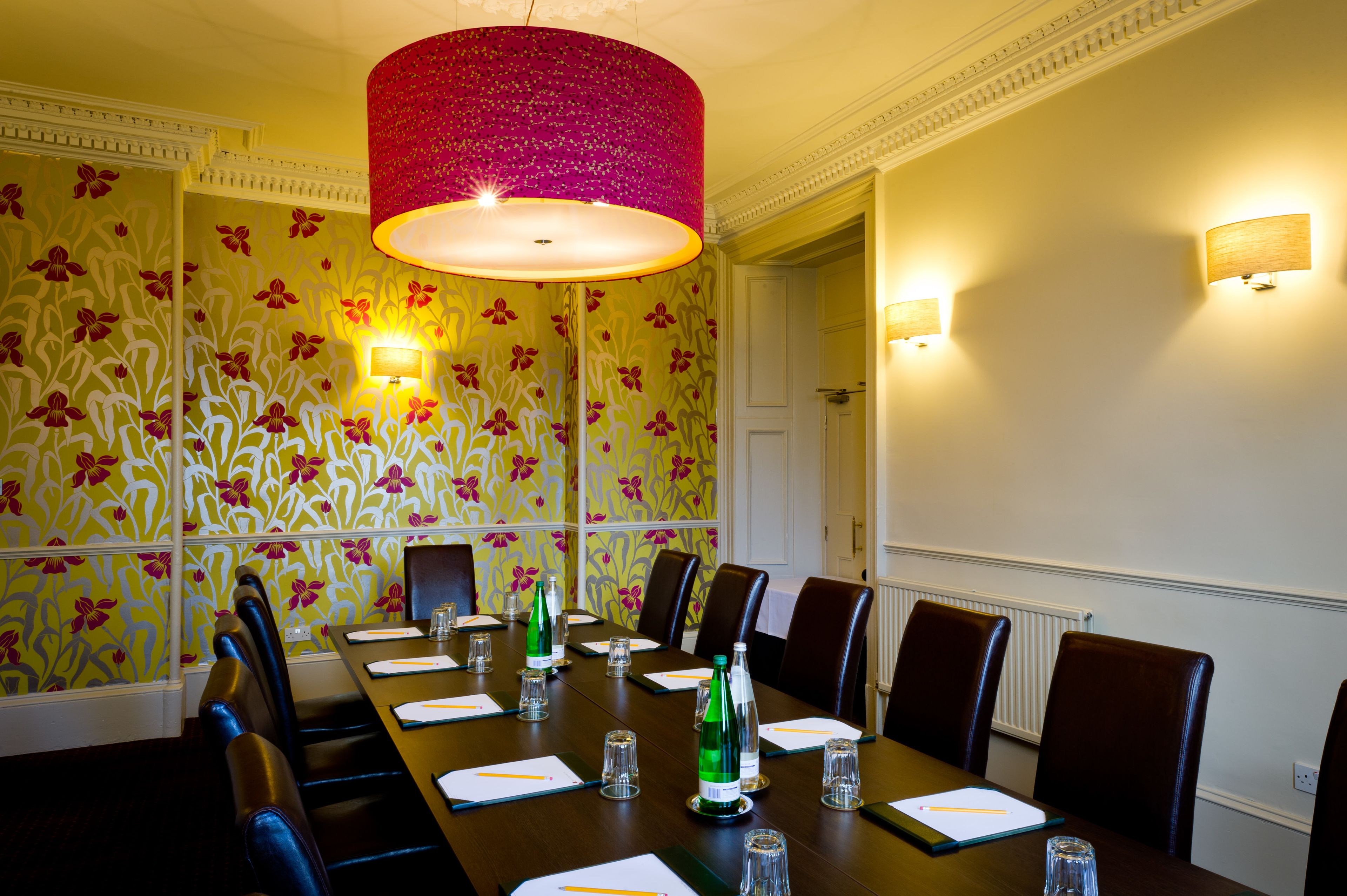 A conference room with a long table, chairs, and floral wallpaper.