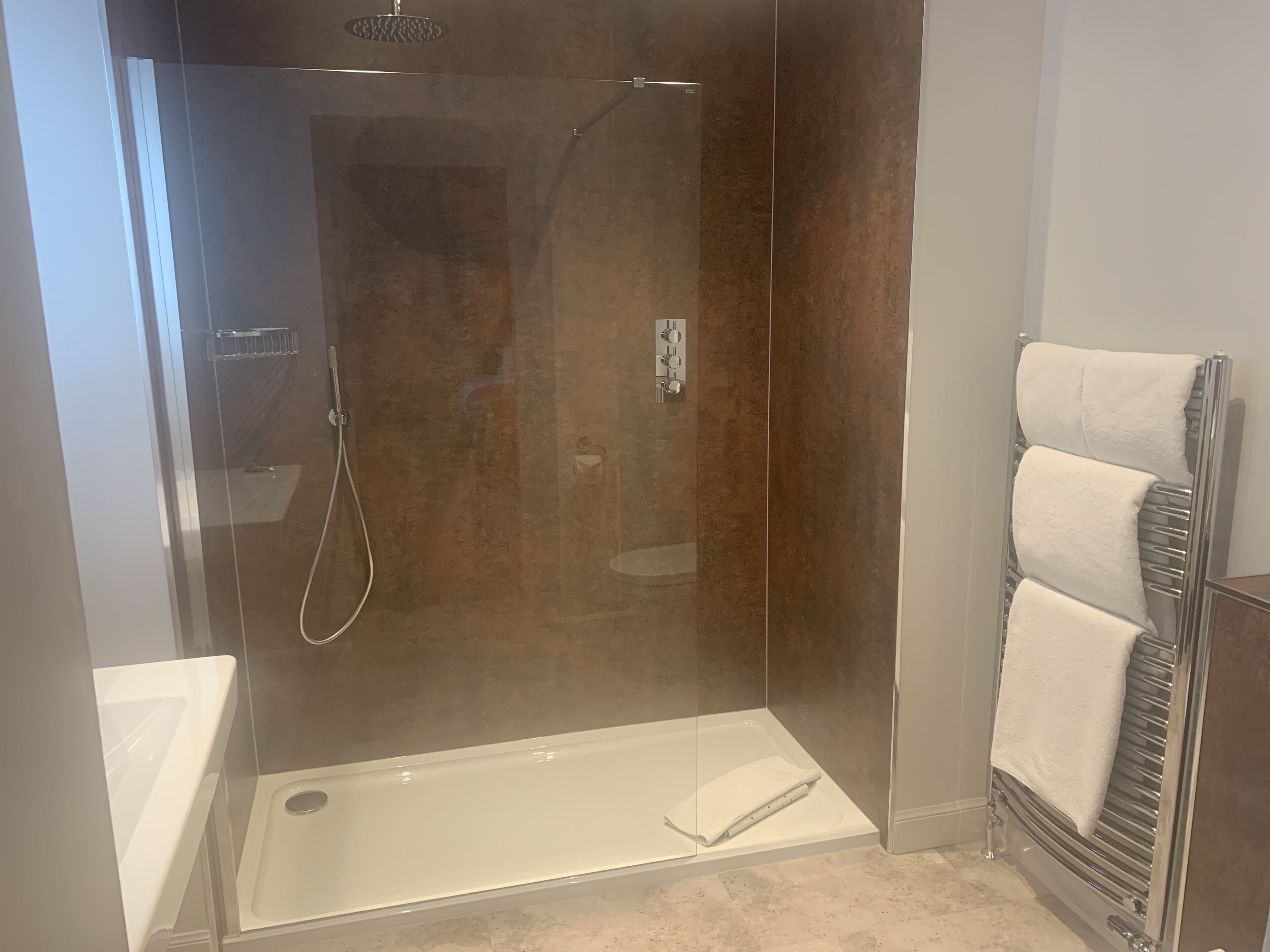 A modern bathroom with a glass-enclosed shower, a white bathtub, and a towel rack.