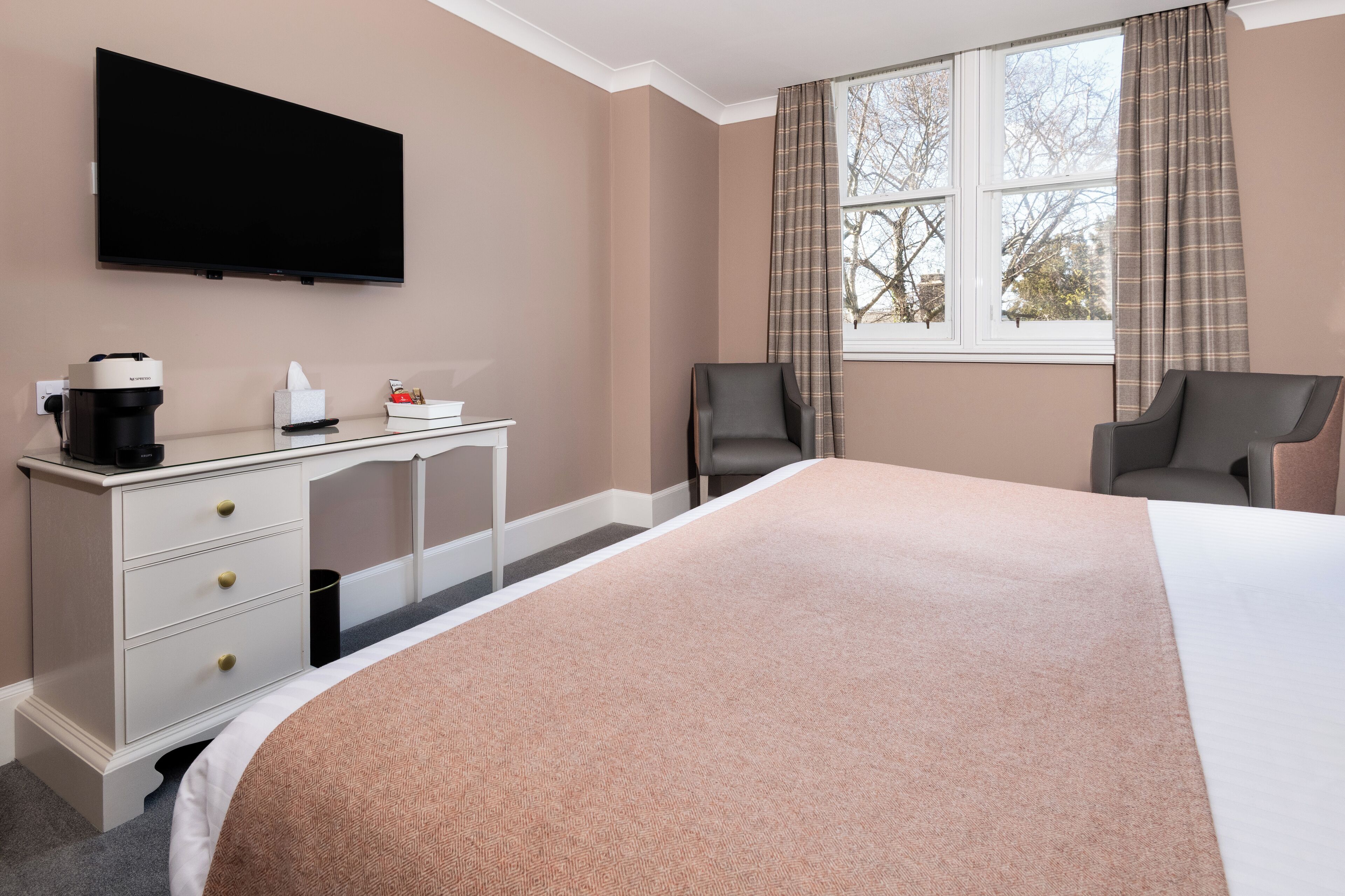 Une chambre d’hôtel avec un grand lit, un bureau avec une machine à café, un téléviseur à écran plat et deux chaises.