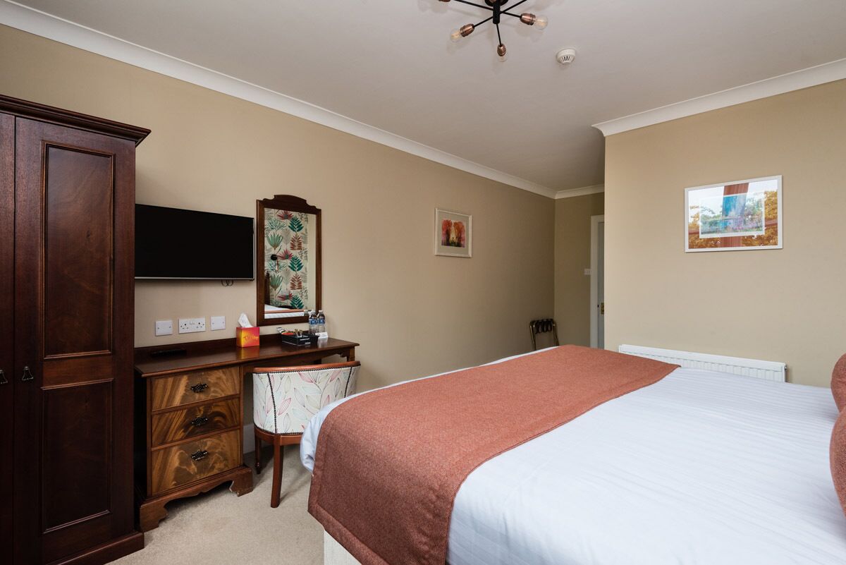 Une chambre à coucher comprenant un lit, une commode, un bureau, une chaise, un téléviseur et un tableau accroché au mur.