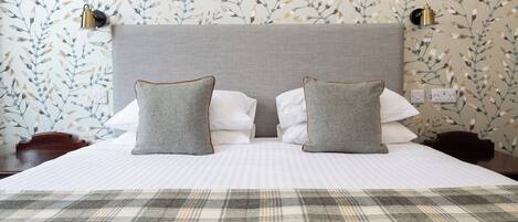 Een keurig opgemaakt bed met een geruite plaid, twee grijze kussens met bruine biezen, en een grijs hoofdbord.