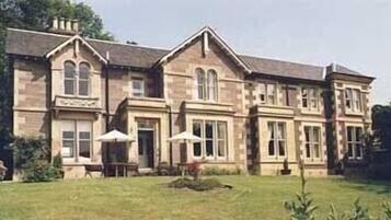 A large, two-story stone building with a symmetrical facade, multiple windows, and a well-maintained lawn in front.