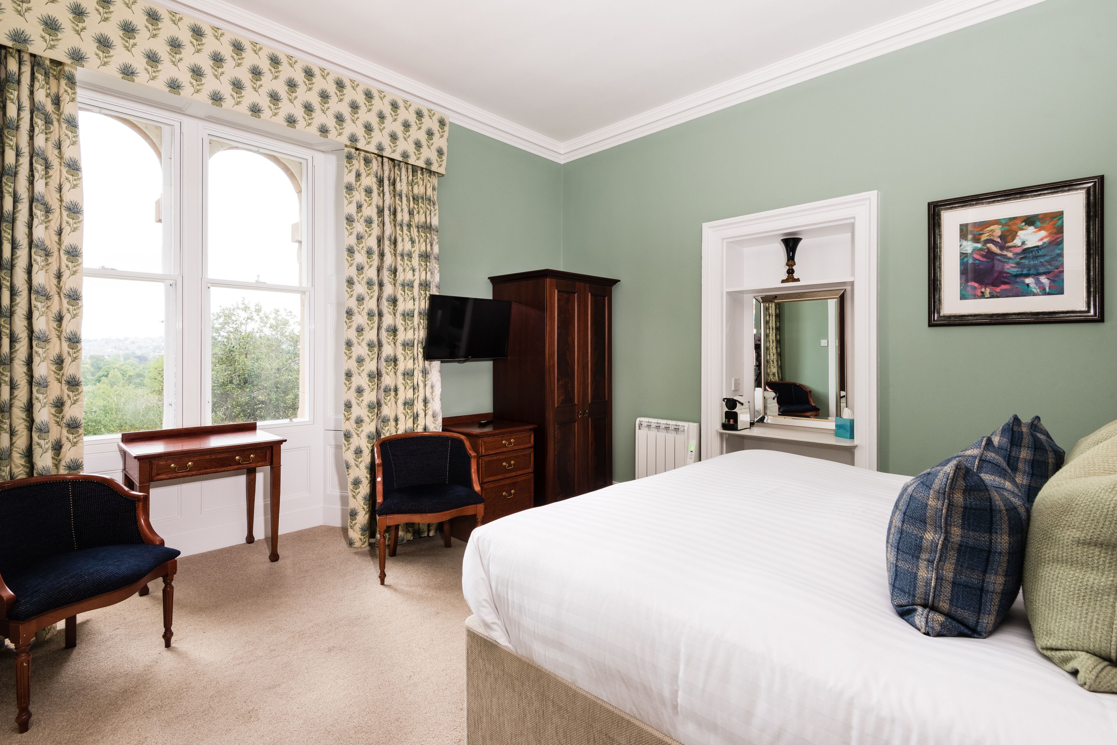Une chambre à coucher avec un grand lit, un bureau avec une chaise, une armoire, une télévision et une fenêtre avec des rideaux.