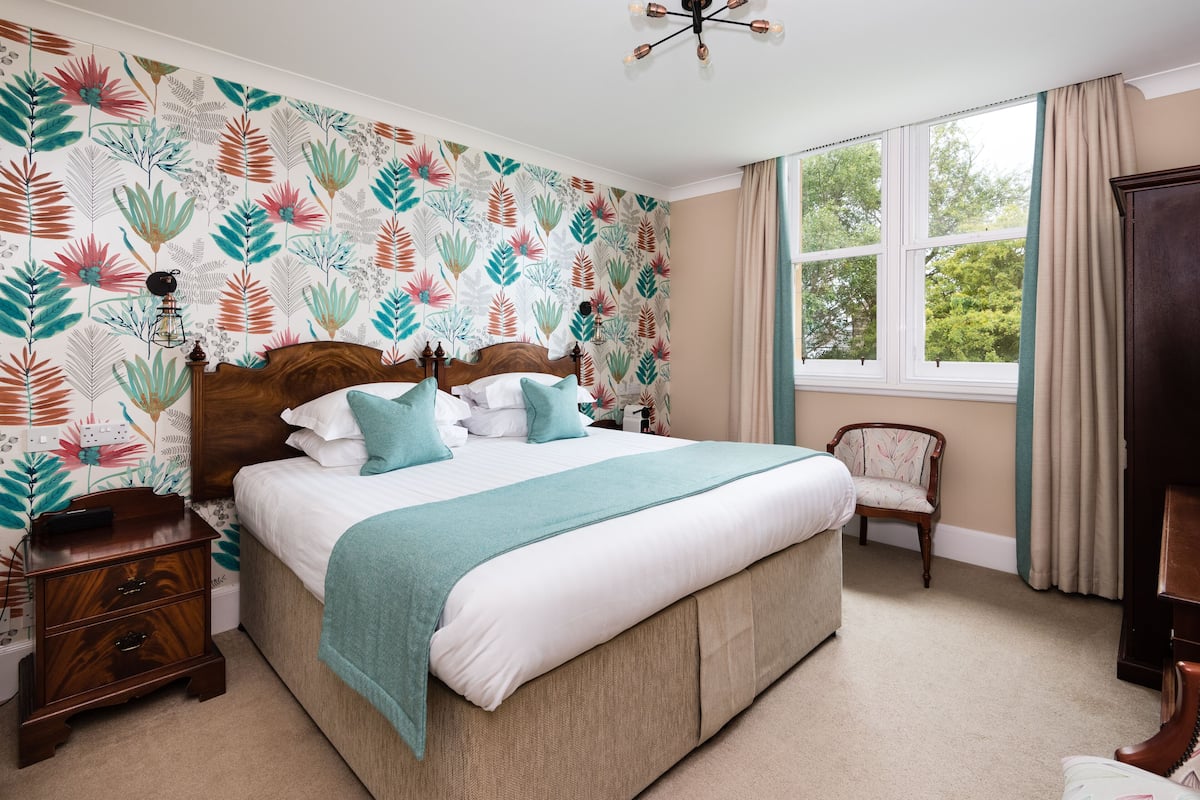 A bedroom with a large bed, a nightstand, a chair, and a window with curtains.