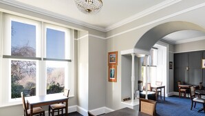 A dining area with a large window, a chandelier, and a view of the outdoors. - Sunbank House Hotel (Perth)