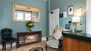 A reception area with a wooden desk, a chair, a console table with magazines, a mirror, and a door. - Sunbank House Hotel (Perth)