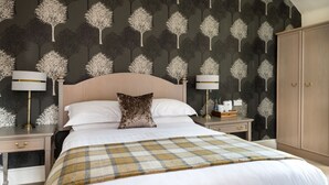 A hotel room with a large bed, two bedside tables, a nightstand, a wardrobe, and a patterned wallpaper. - Sunbank House Hotel (Perth)