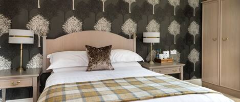 A hotel room with a large bed, two bedside tables, a nightstand, a wardrobe, and a patterned wallpaper.