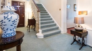 A staircase with a white railing, a blue and white vase on a table, and a lamp on a side table. - Sunbank House Hotel (Perth)