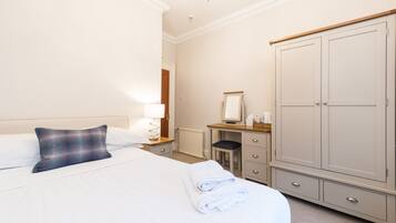 A hotel room with a bed, a bedside table with a lamp, a dresser, and a large wardrobe.