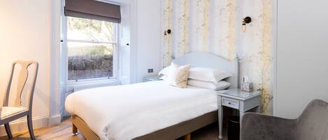 A bedroom with a bed, a chair, a nightstand, and a window with a view of the outside.