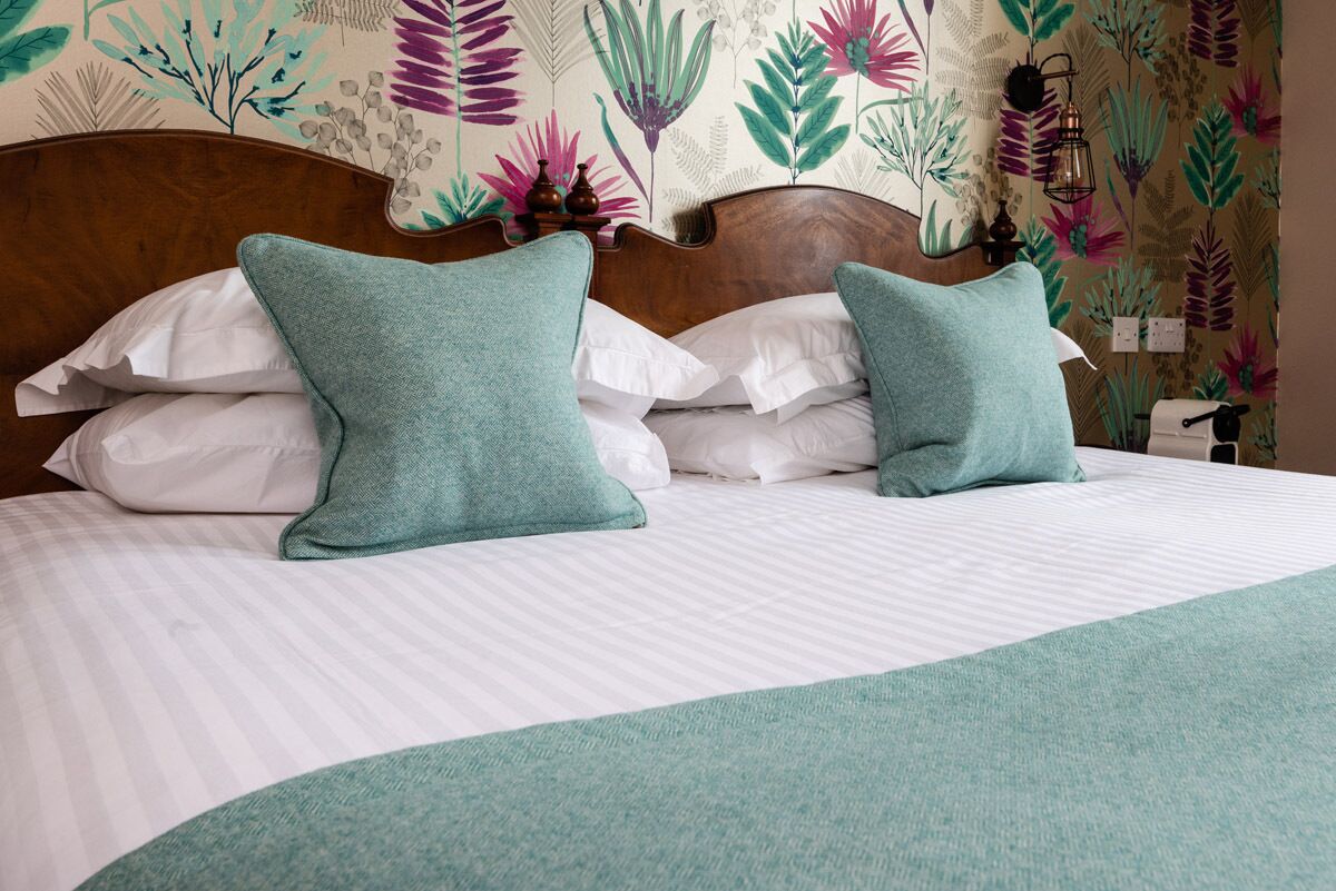 Una cama bien hecha con una colcha blanca a rayas y dos almohadas color turquesa.
