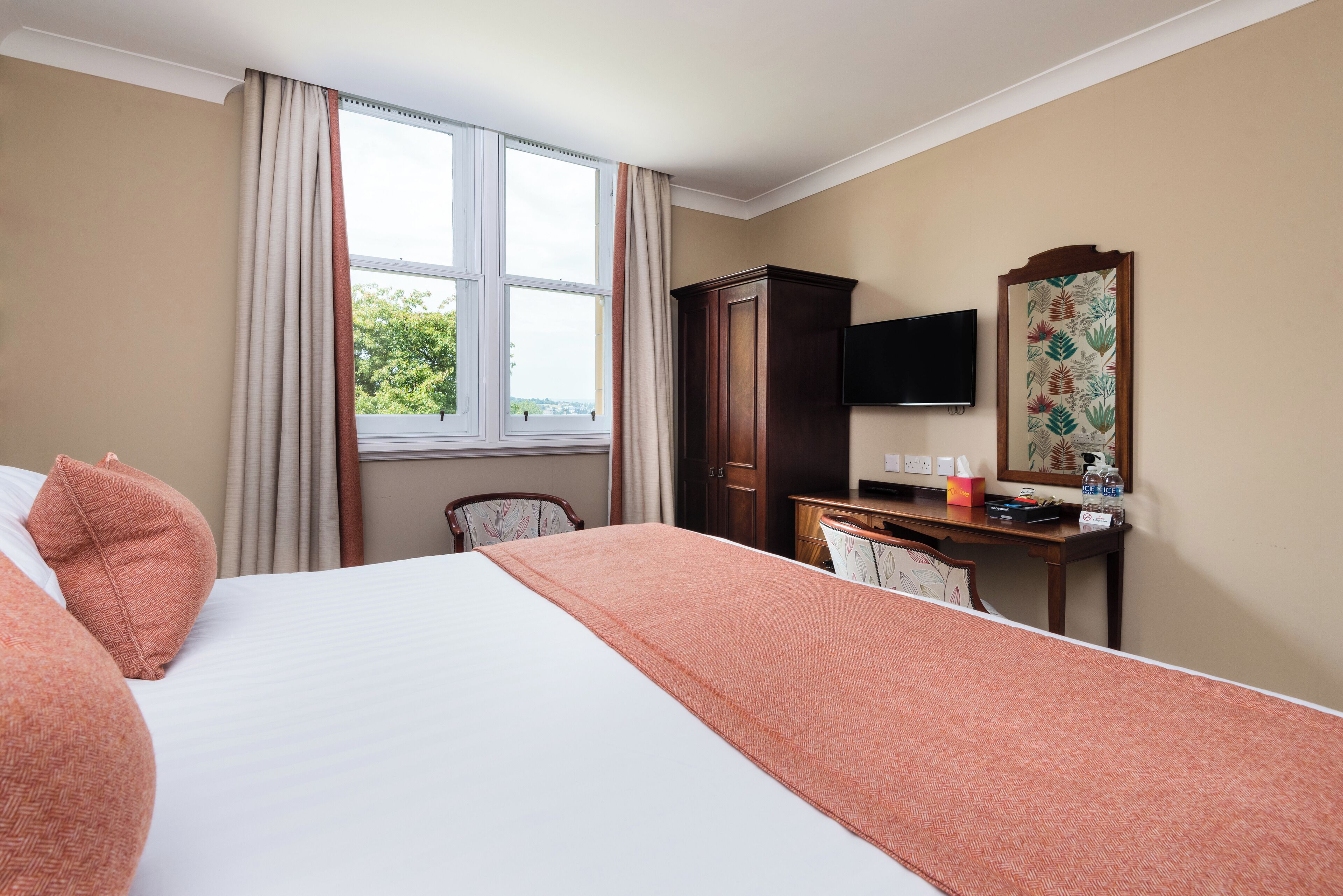 A hotel room with a bed, a desk, a chair, a television, and a window with curtains.