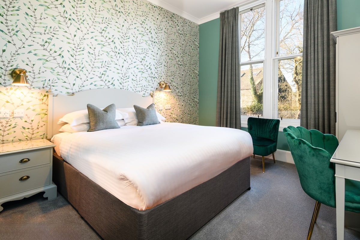 A neatly arranged bedroom with a large bed, bedside lamps, a desk, and a chair.