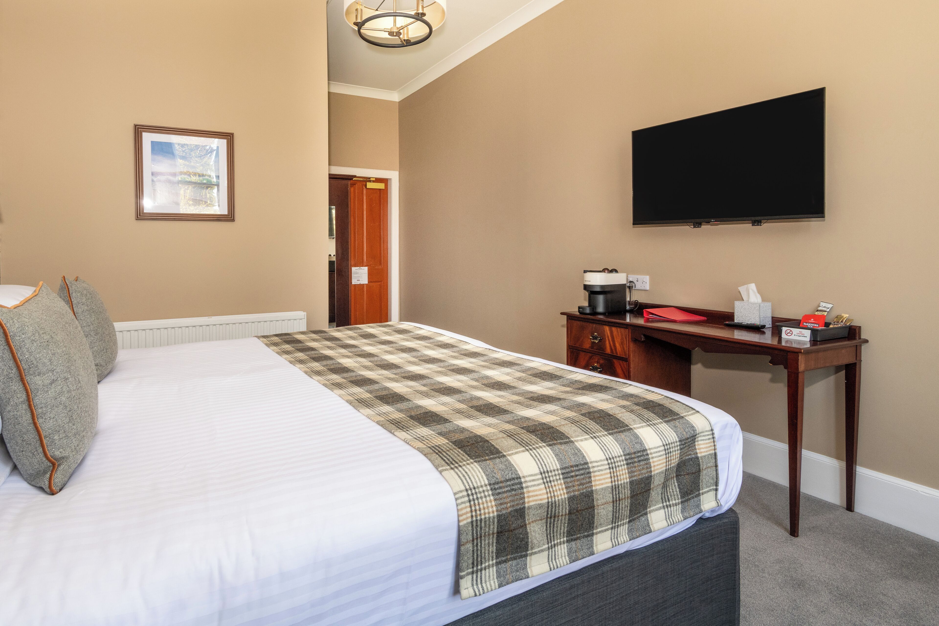A hotel room with a bed, a desk, a television, and a door.
