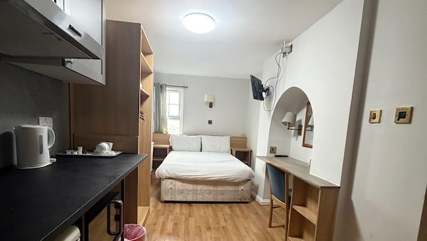 A compact room with a kitchenette, a bed, a desk, and a mirror. - Crescent Hotel (Reading)