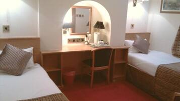 Una camera d'albergo con una scrivania, due letti, una sedia e uno specchio.