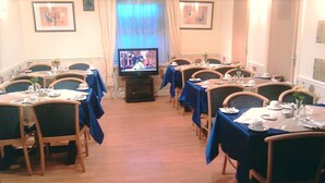 A dining area with tables set for meals, a television in the center, and framed pictures on the walls. - Crescent Hotel (Reading)