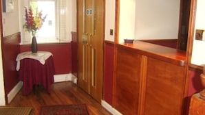 A hallway with a wooden door, a small table with a vase of flowers, and a mirror on the wall. - Crescent Hotel (Reading)