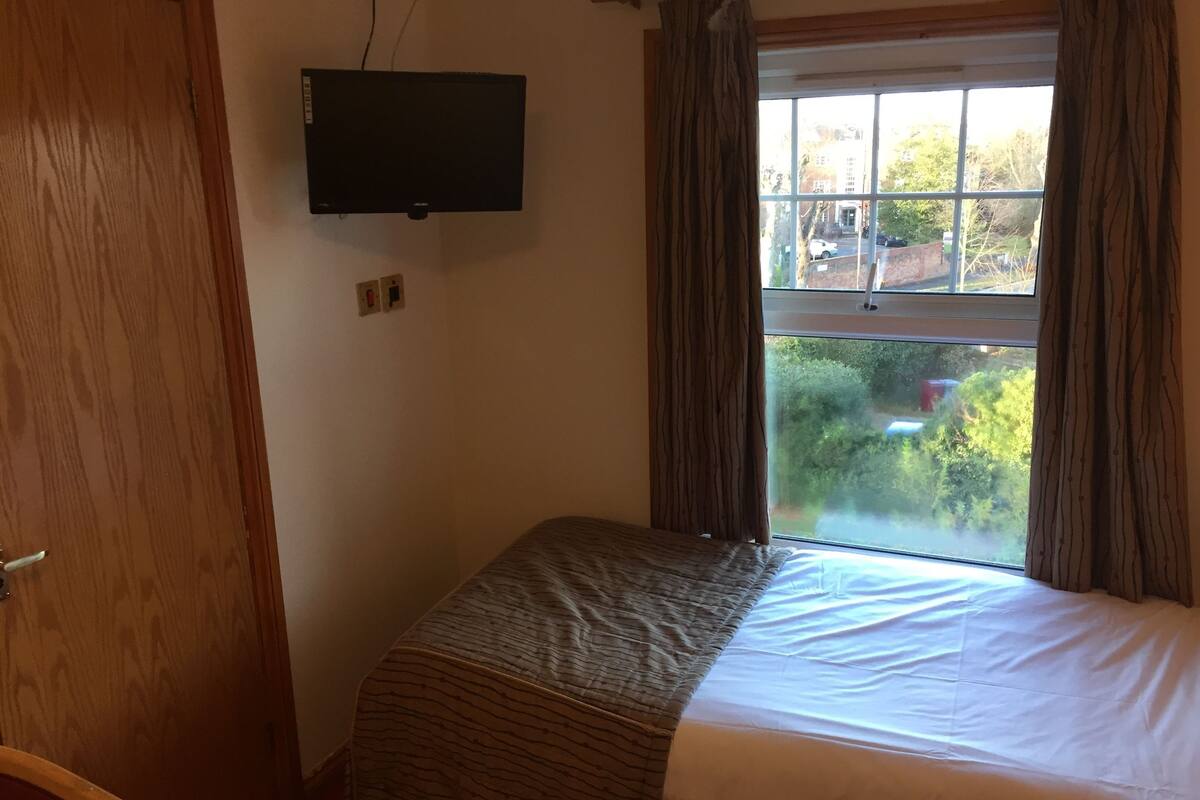 A bedroom with a bed, a television mounted on the wall, and a window with curtains.