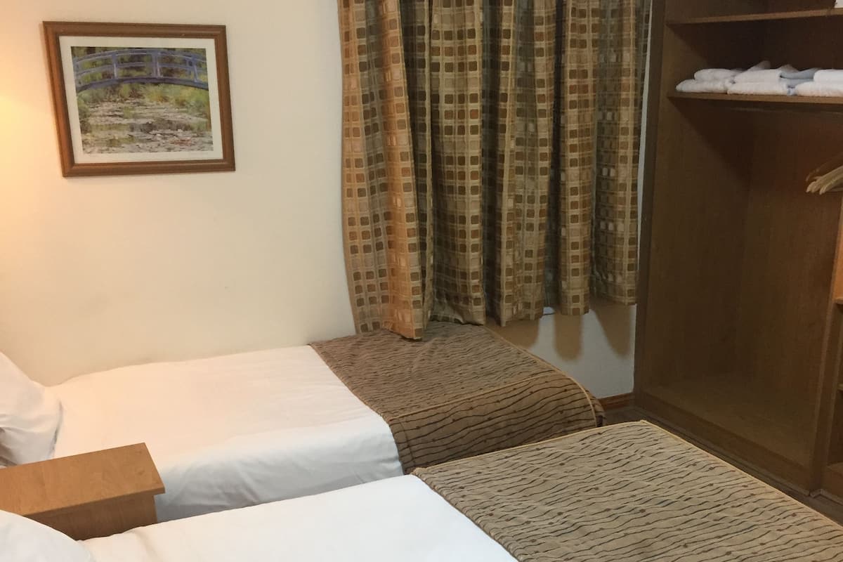 A room with two beds, a wooden wardrobe, a painting on the wall, and patterned curtains.