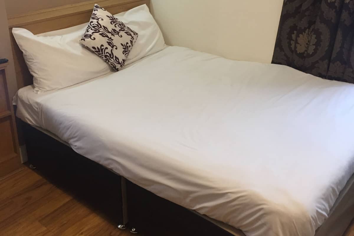 A single bed with white bedding, a patterned pillow, and a framed picture on the wall.