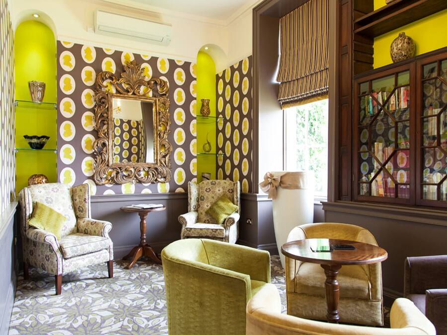 A room with patterned wallpaper, a large mirror, and multiple chairs.