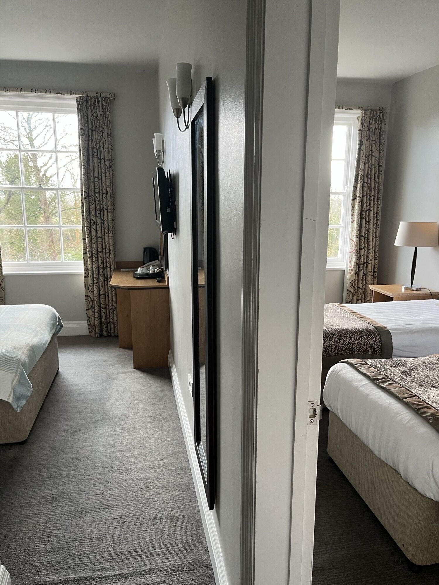 A hotel room with two beds, a desk with a television, and a window with curtains.
