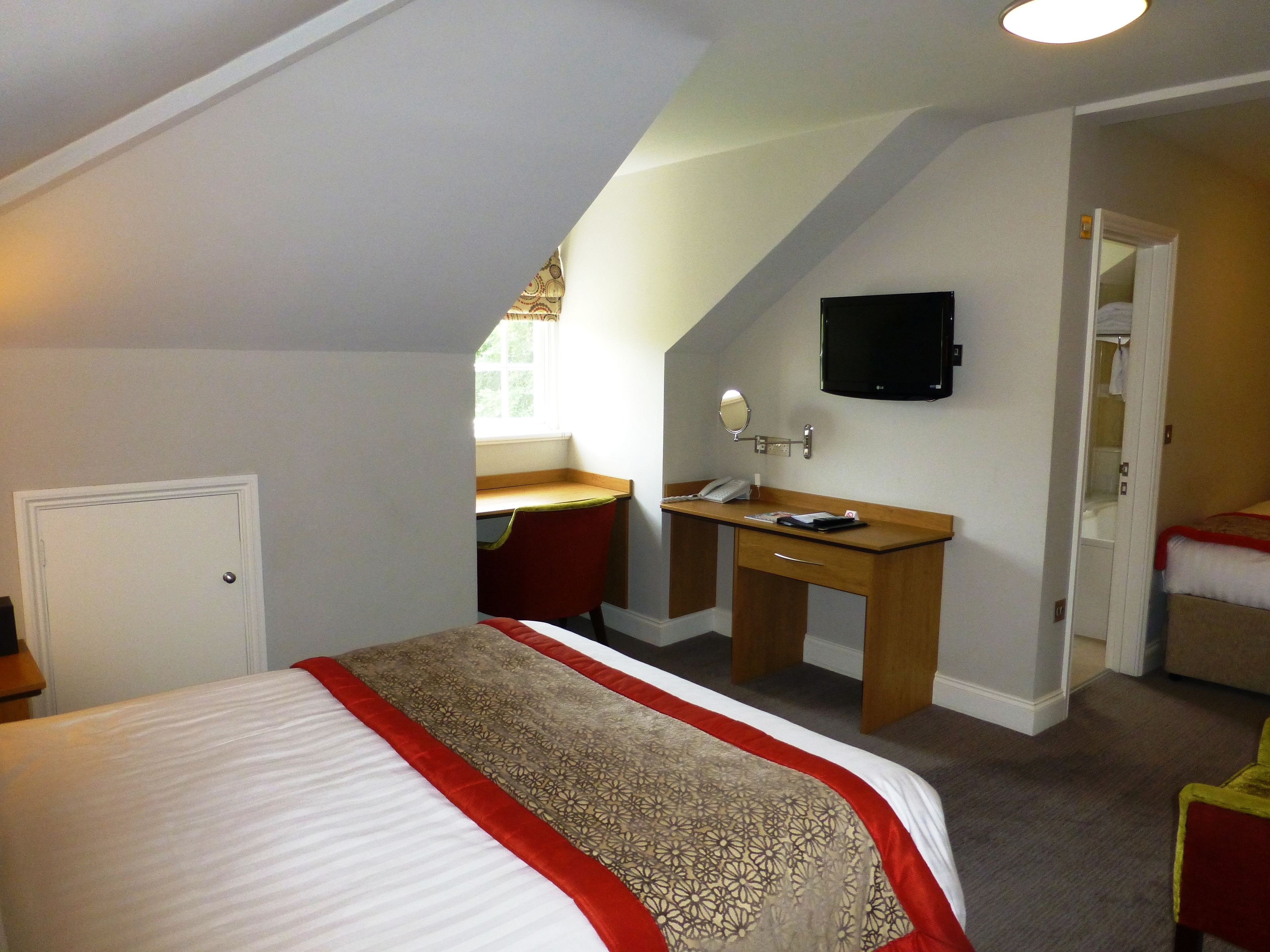 A bedroom with a bed, a desk, a mirror, and a television.