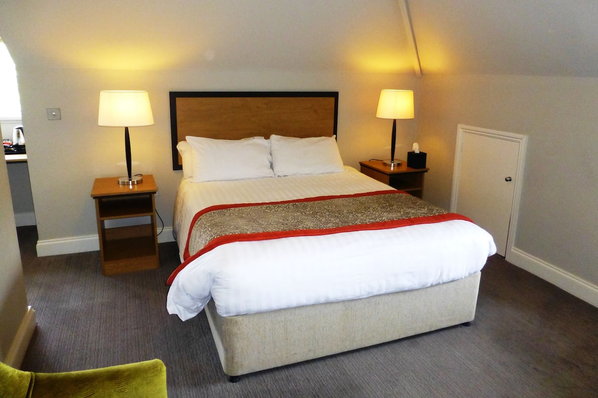 A neatly made bed with a wooden headboard, two bedside tables with lamps, a bedside table with a tissue box, and a door to the right.