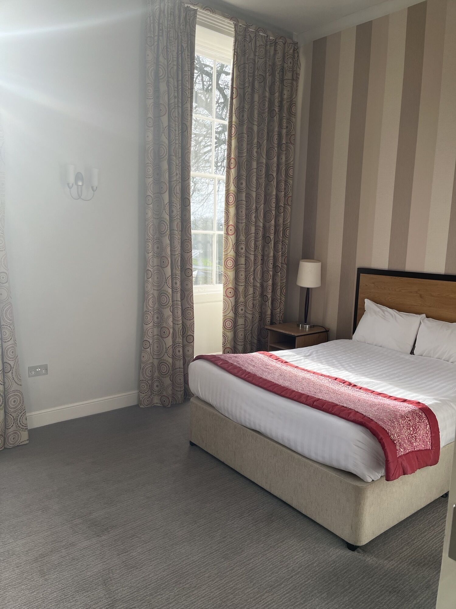A hotel room with a large bed, a bedside table with a lamp, and a window with curtains.