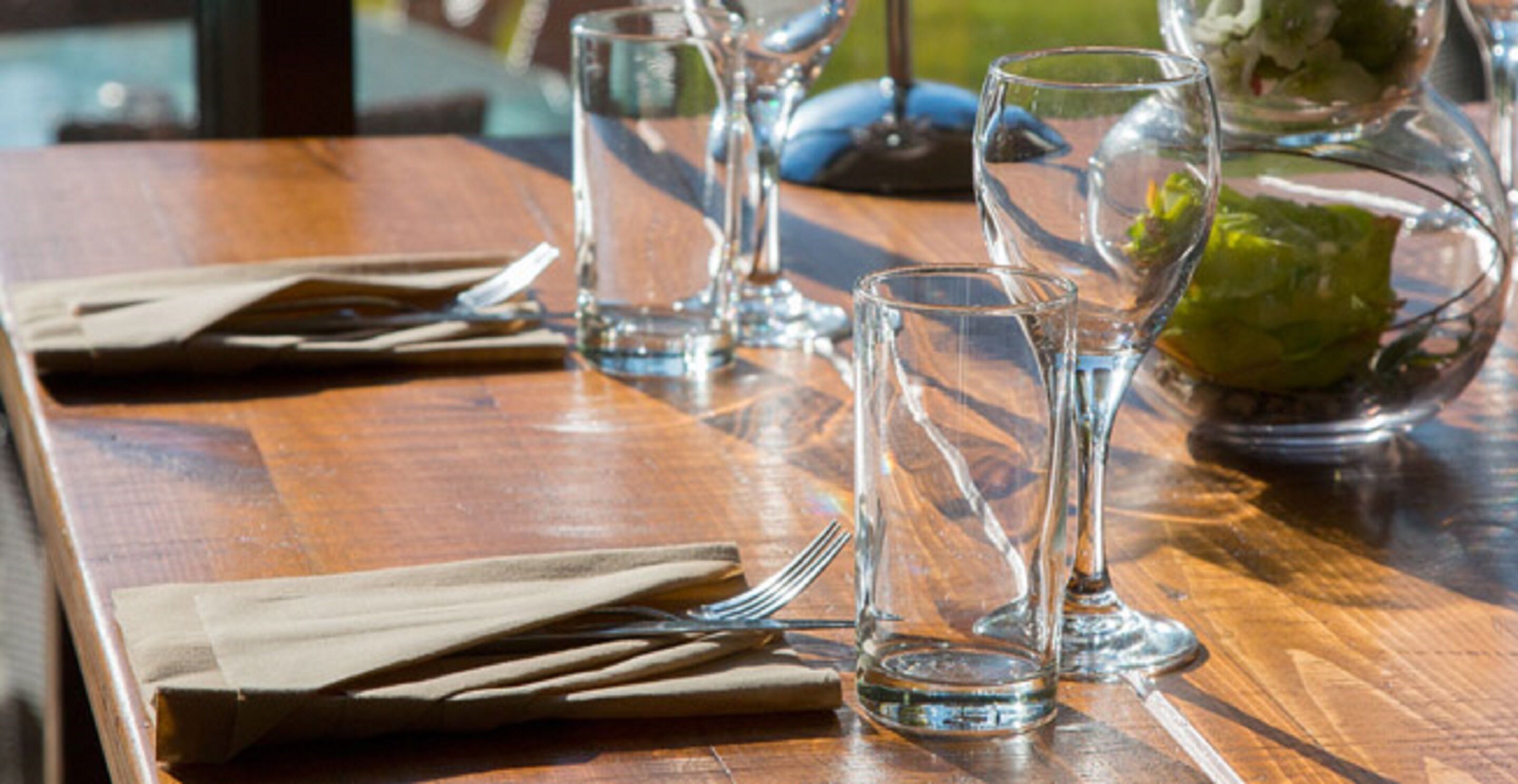 Een houten tafel met helder glaswerk en een saladekom met groene salade.