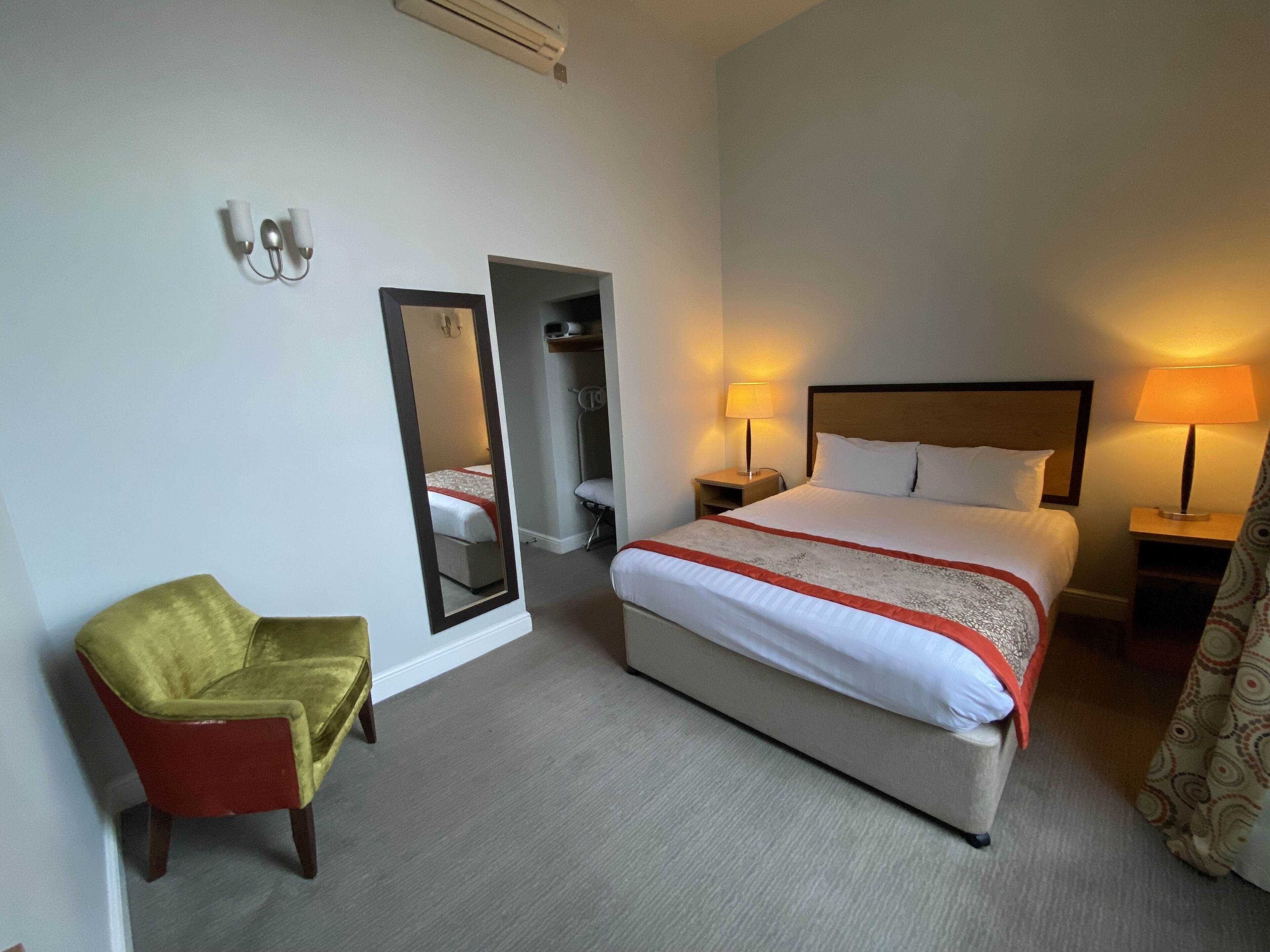Une chambre d’hôtel comprenant un lit, des lampes de chevet, un miroir, une chaise et une armoire.