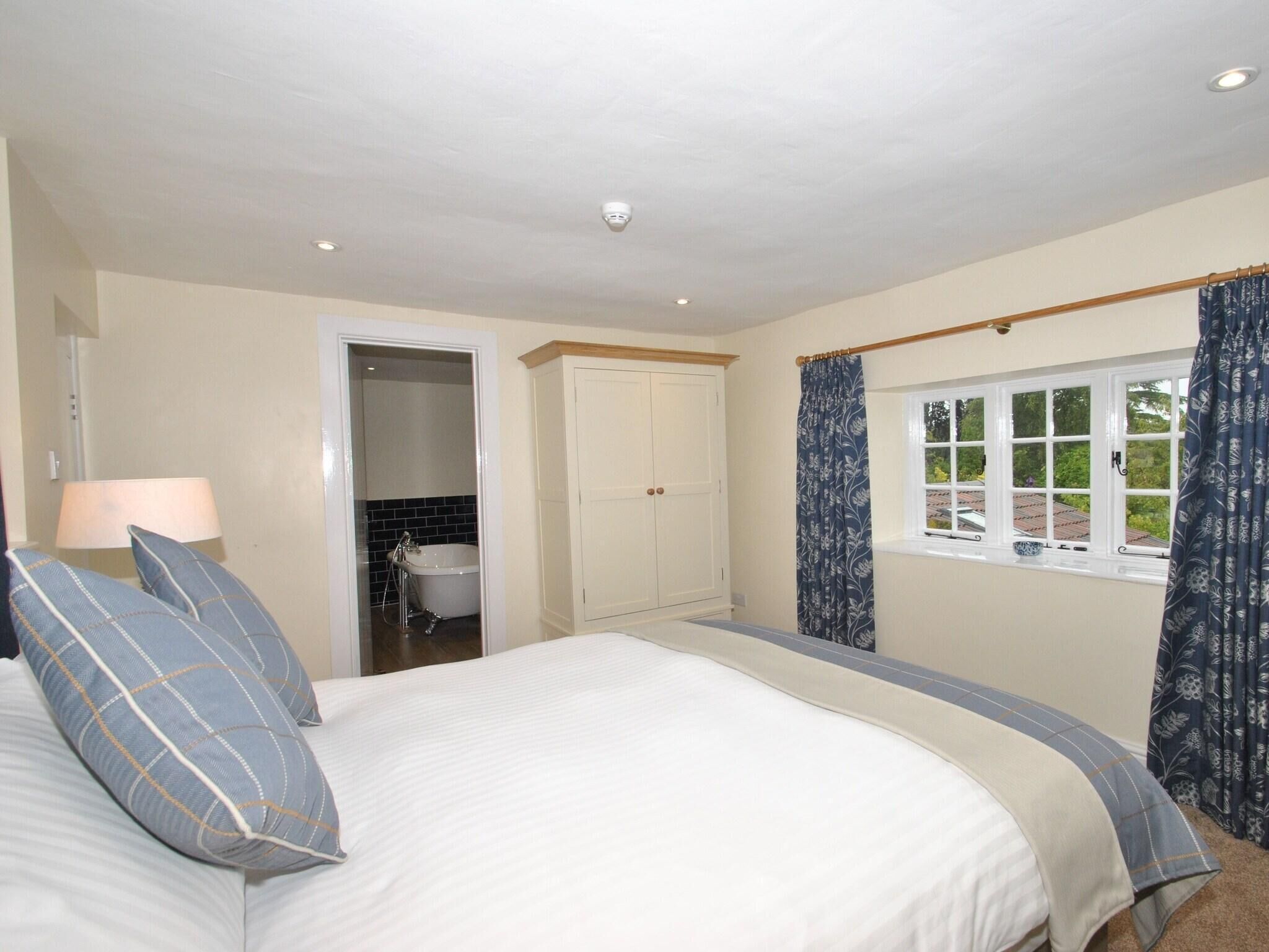 A bedroom with a bed, a wardrobe, a window with curtains, and a bathroom visible through an open door.
