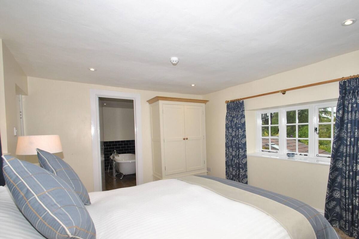 A bedroom with a bed, a wardrobe, a window with curtains, and a bathroom visible through an open door.