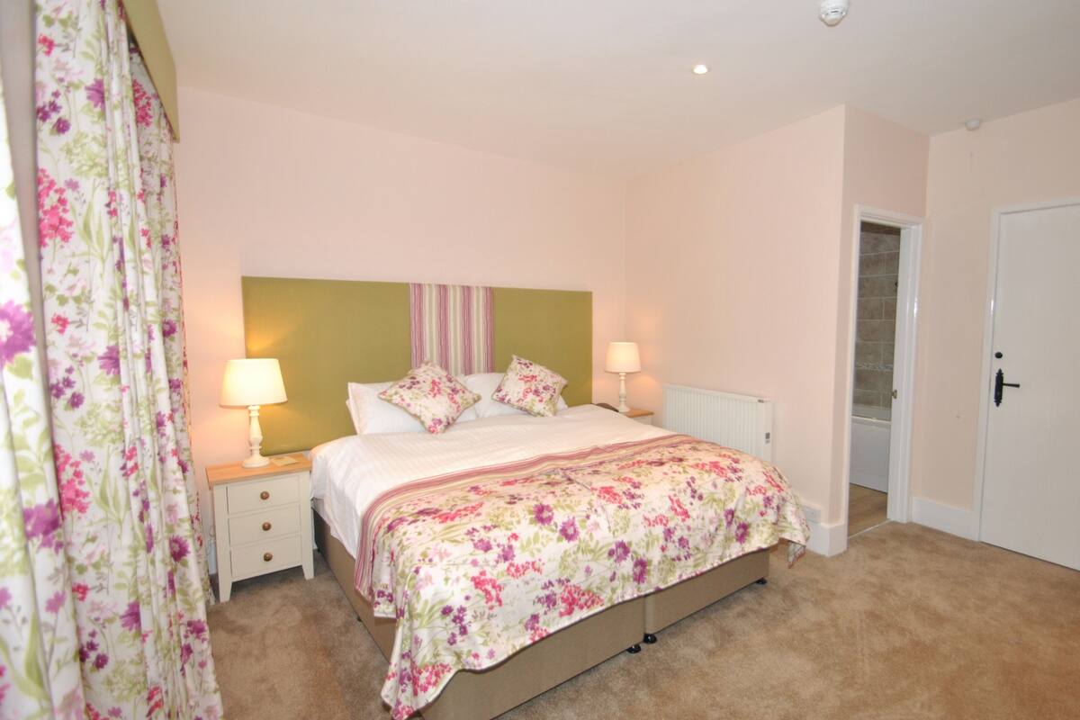 A bedroom with a bed, two bedside tables, a nightstand, a radiator, and a door.