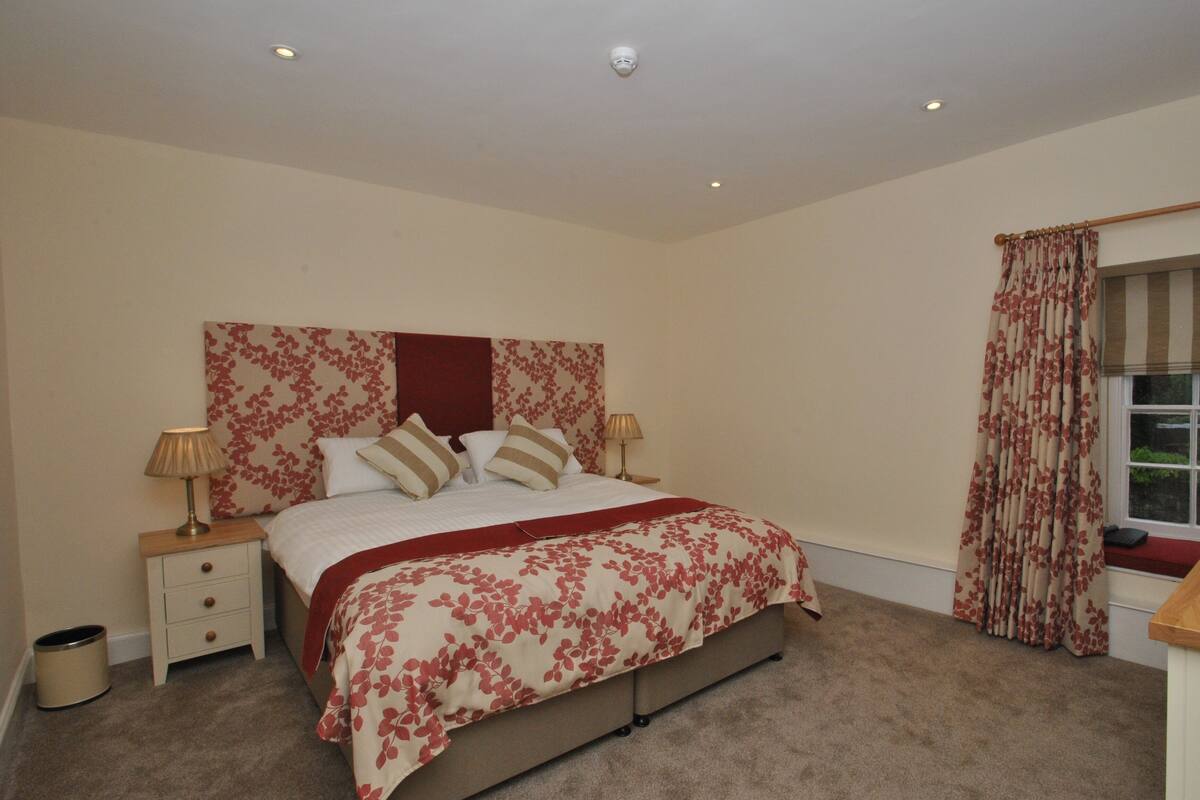 A bedroom with a bed, nightstands, a window with curtains, and a ceiling light.