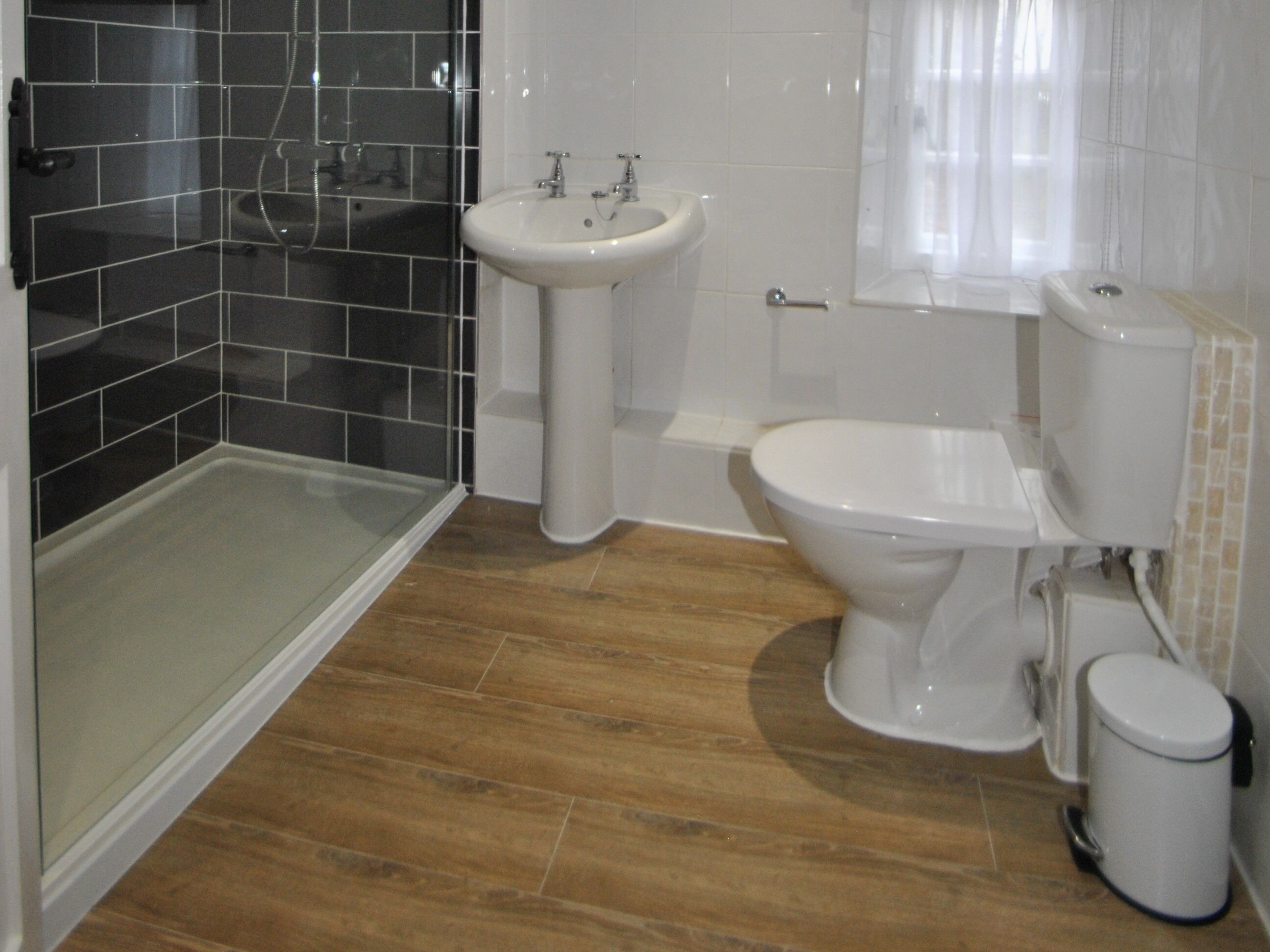 A bathroom with a glass shower enclosure, a pedestal sink, a toilet, and a bidet.