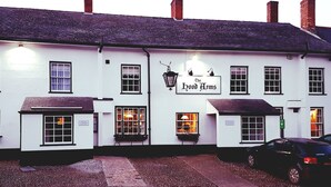 A white building with a sign reading "The Hood Arms." It has multiple windows, a brick chimney, and a car parked in front. - The Hood Arms (Bridgwater)