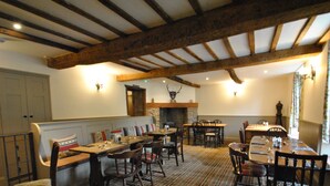 A dining area with wooden tables and chairs, a fireplace, and a checkered floor. - The Hood Arms (Bridgwater)