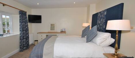 A bedroom with a bed, bedside tables, a desk, a television, and a window.