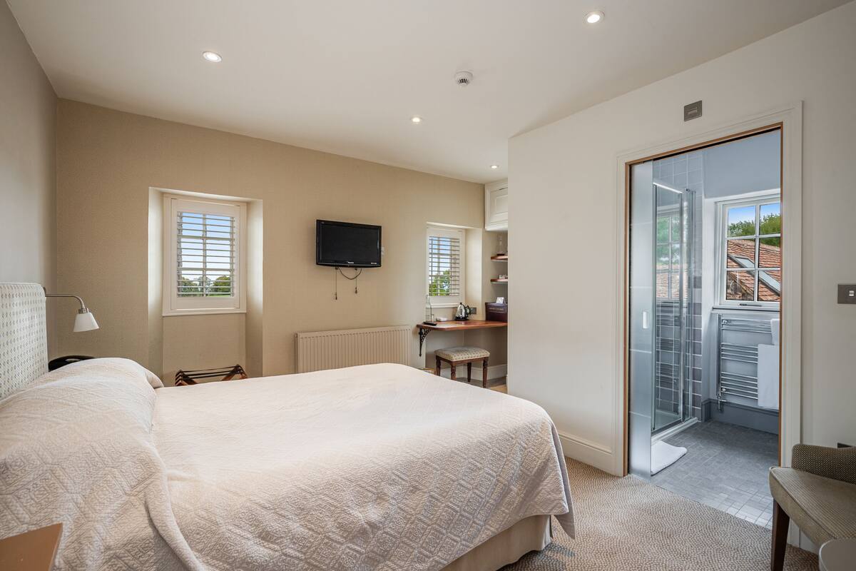 A bedroom with a large bed, a desk, a television, and a sliding glass door to a balcony.