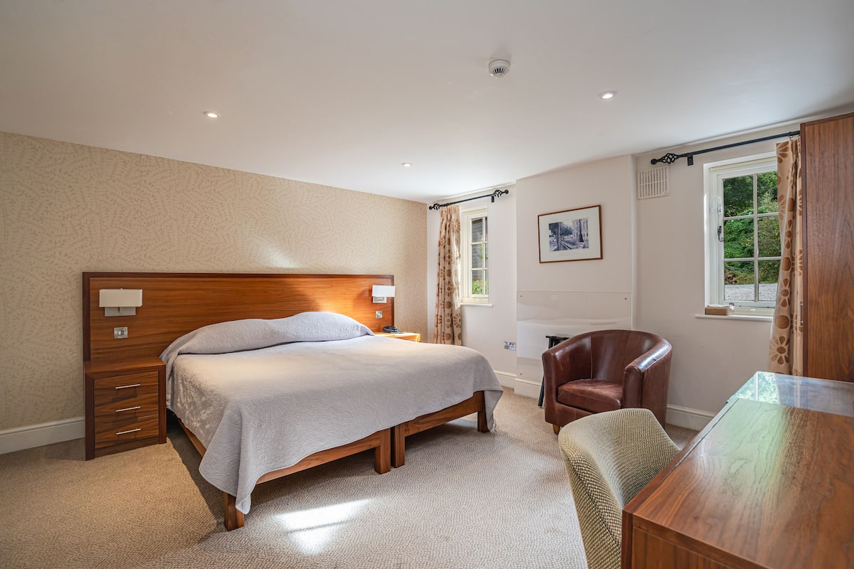 A bedroom with a wooden bed, a leather armchair, a wooden desk, and a window with curtains.