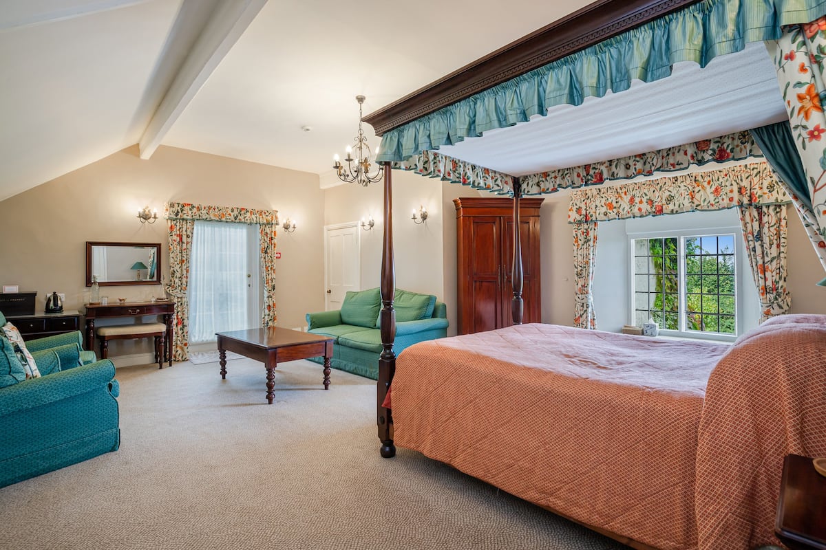 A bedroom with a four-poster bed, a green sofa, a wooden desk, and a chandelier.