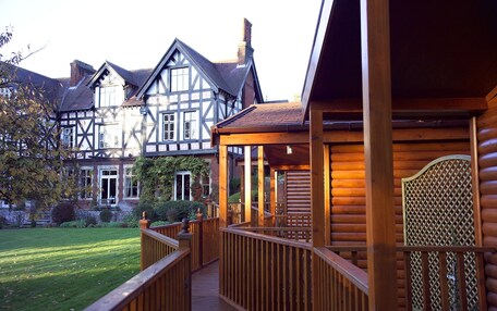 A wooden deck leading to a house with a traditional half-timbered facade, a well-maintained lawn, and a brick chimney.