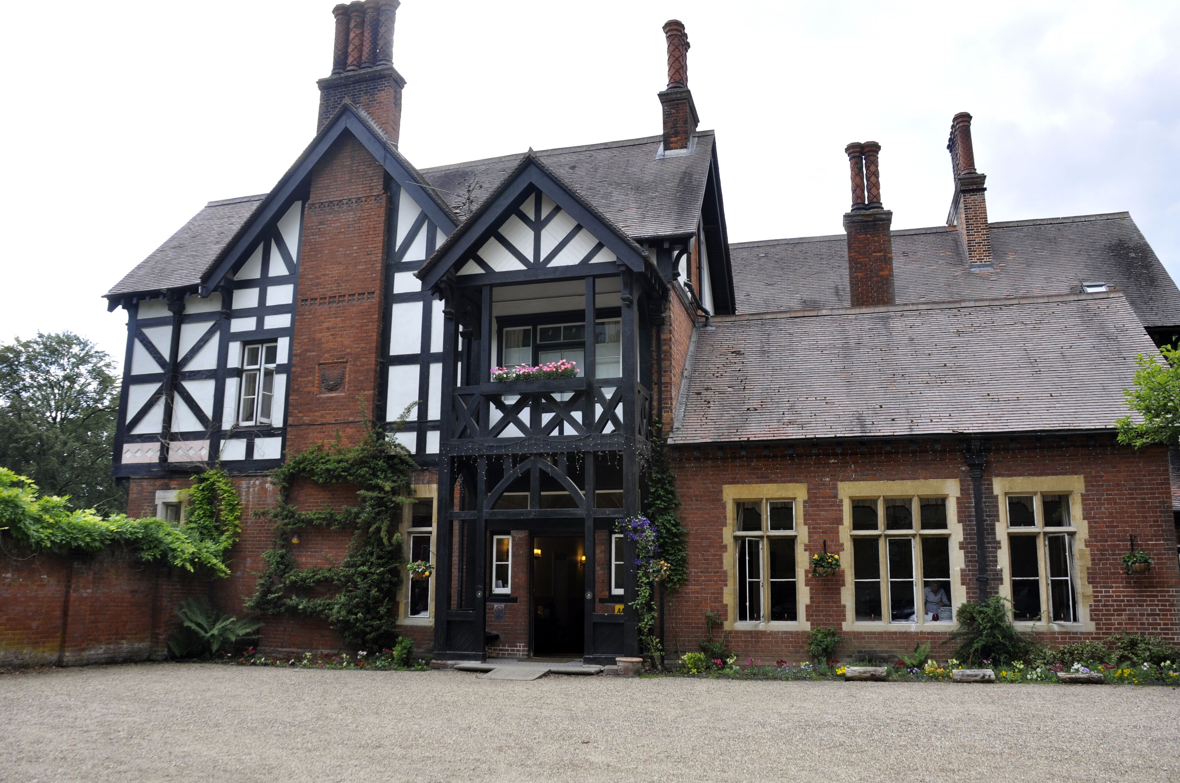 Un bâtiment traditionnel de style Tudor, caractérisé par une façade noire et blanche bien visible, de nombreuses cheminées et une entrée accueillante agrémentée d’une jardinière.