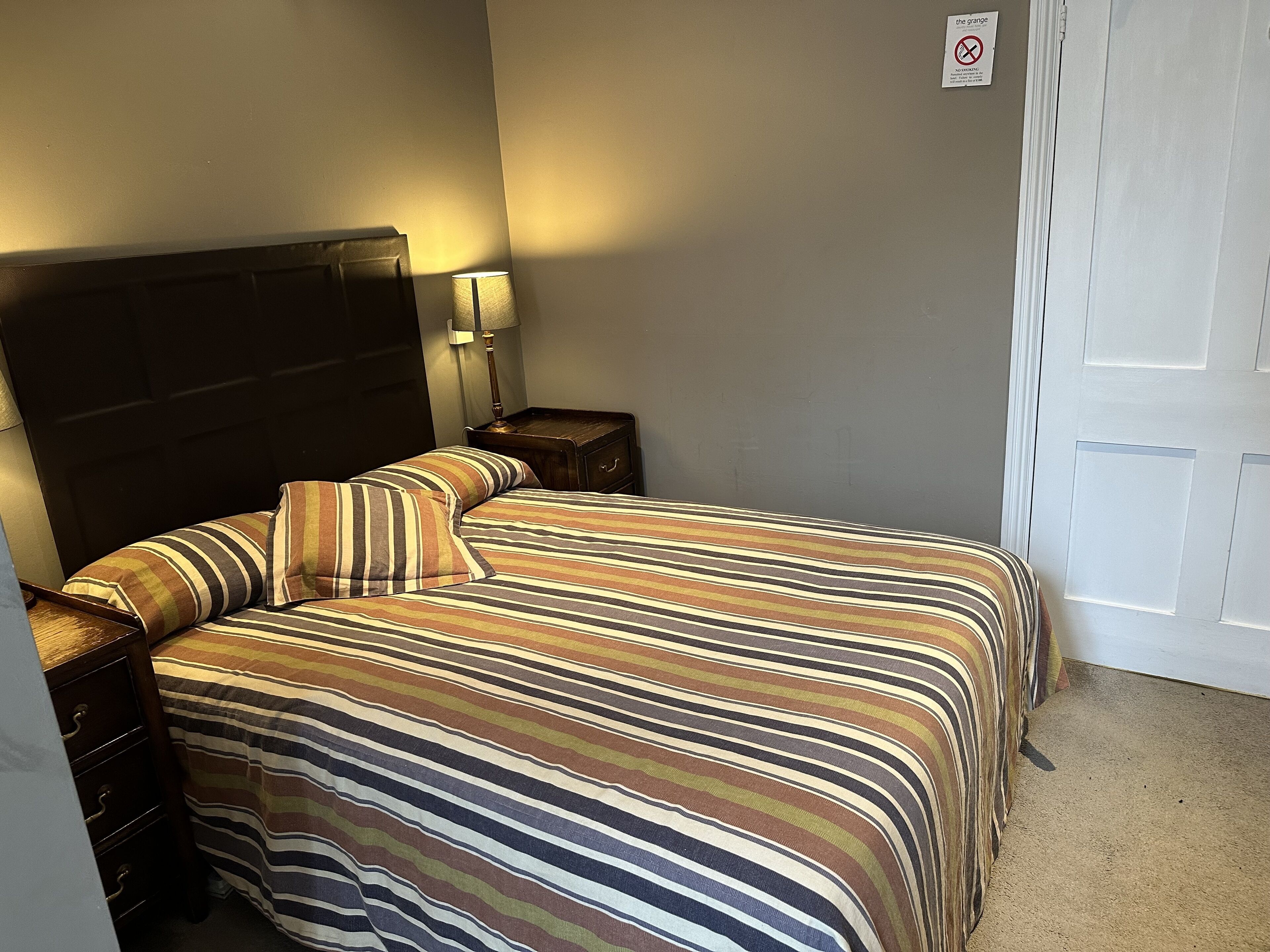 A neatly made bed with striped bedding, a bedside lamp, and a nightstand.